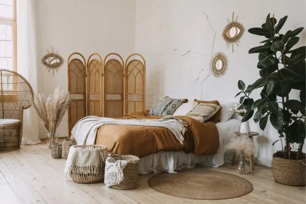 Bohemian-style bedroom with a rattan headboard, earth-toned bedding, round jute rug, and lush indoor plants, showcasing a popular global interior design trend.