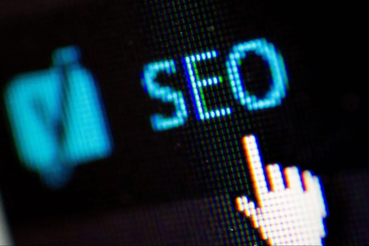 Close-up view of a computer screen showing the word 'SEO' with a hand cursor icon pointing at it. The image highlights the concept of search engine optimization.