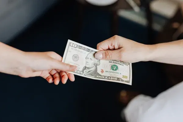 hands of 2 people, one giving cash while the other receiving the cash