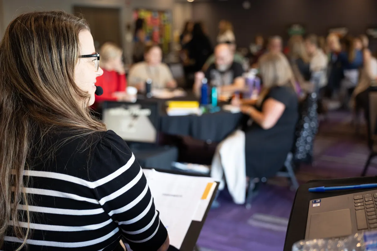 Kim and Kat presenting to attendees at the Profitable Speaker Bootcamp, standing near a projector screen and podium.