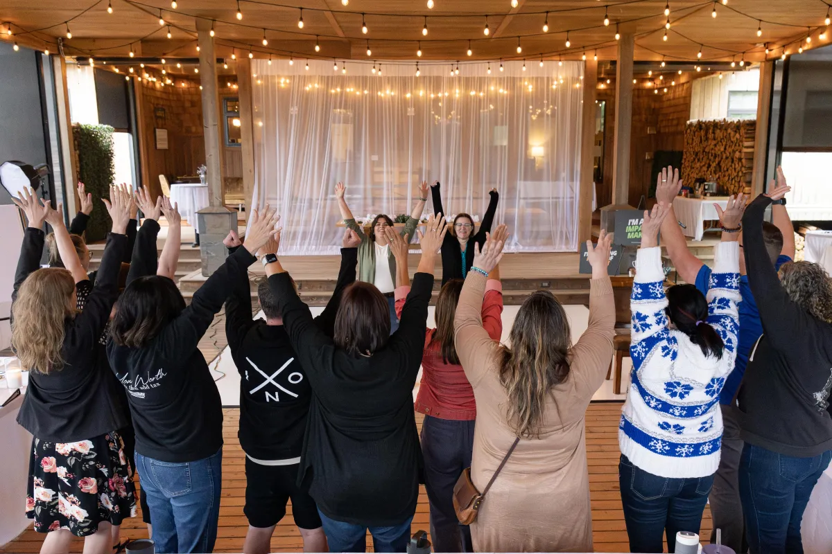 Kim and Kat presenting on stage at the Profitable Speaker Bootcamp with attendees seated and event signage visible.