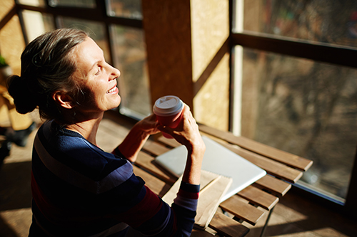 Woman standing by a window in soft natural light, looking outward with a calm, reflective expression, conveying emotional regulation, restraint, and quiet confidence.