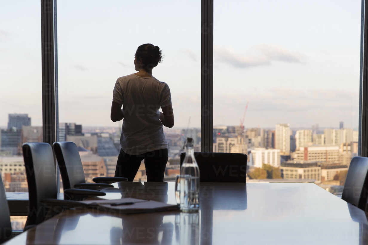 A professional standing near a window in a softly lit office, appearing thoughtful and reflective, representing the unseen challenges many people carry in the workplace.