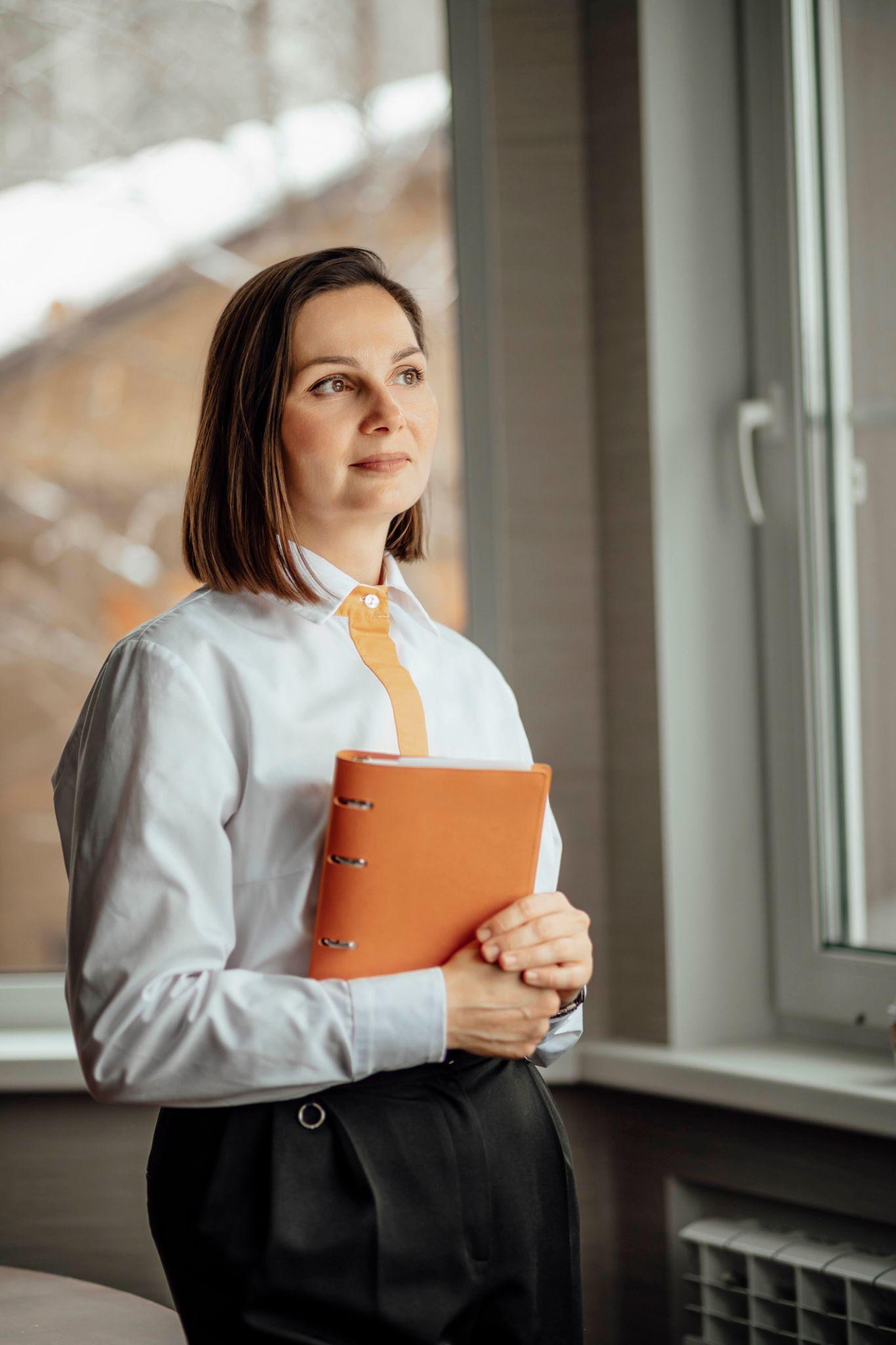 Woman standing calmly by a window in natural light, representing grounded leadership and emotional regulation.