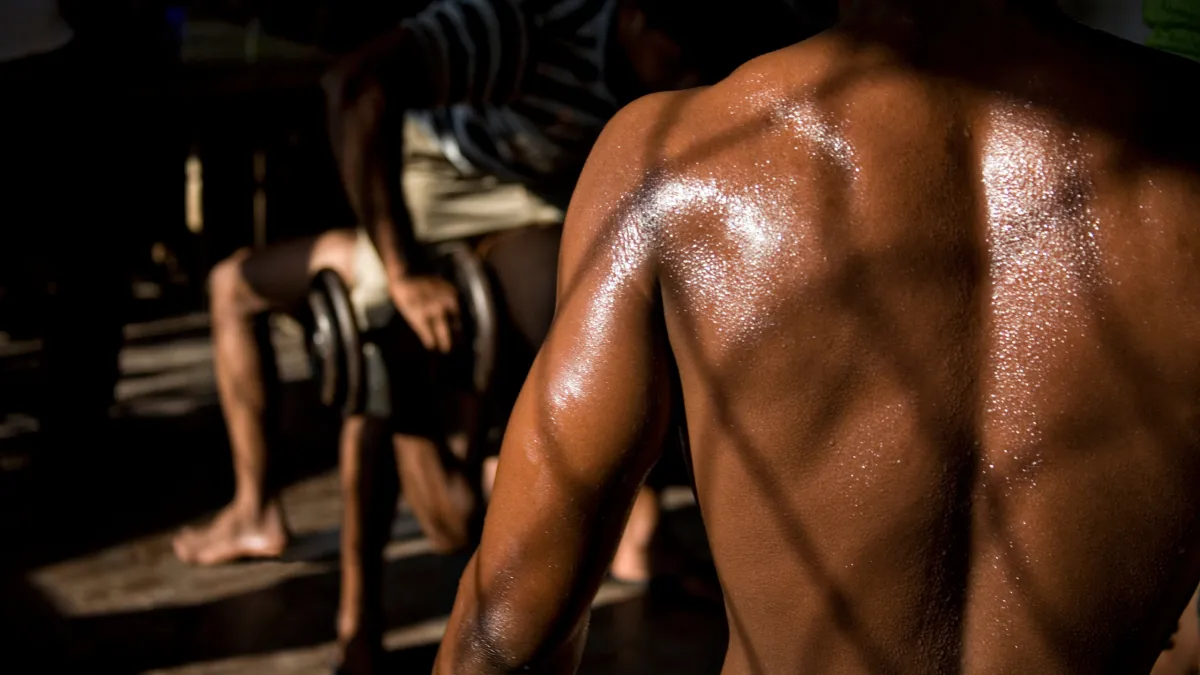 A man standing in the shadow of a building, sweat glistening on his face.