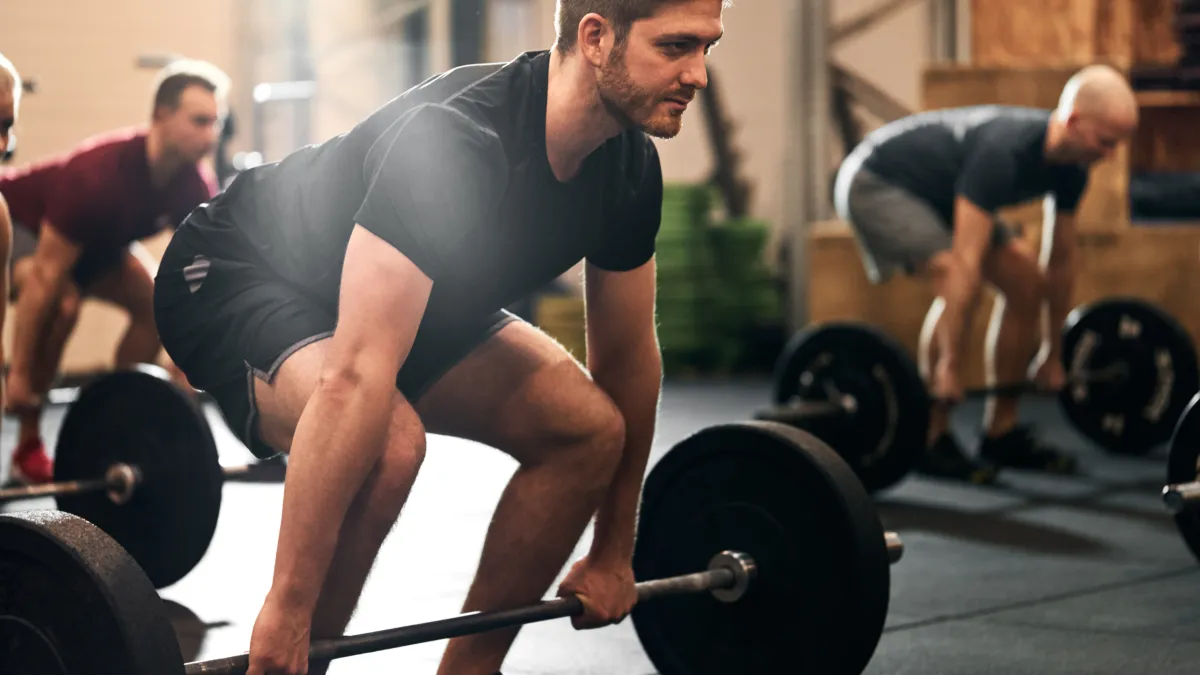 A group of men performing squats in a gym, focusing on their lower body strength and fitness.