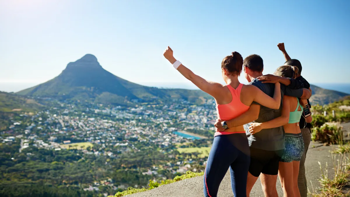 Four friends celebrating their achievement on top of a mountain, joyfully extending their arms.