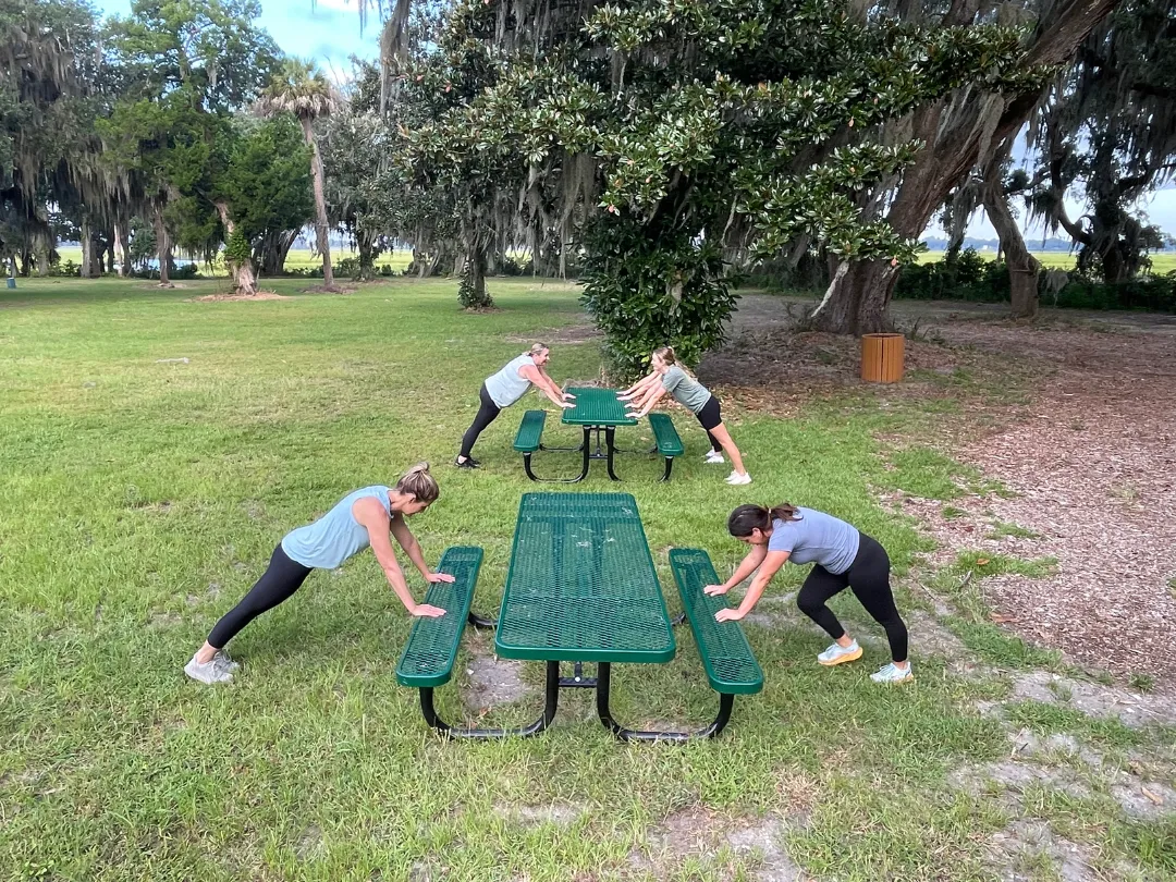 Women doing planks outside in a peaceful natural setting, showcasing the mental health benefits of exercise.