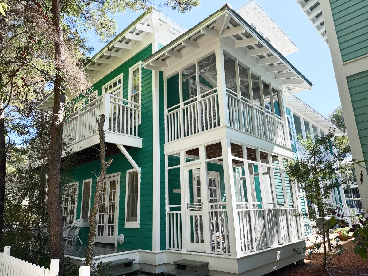 Bright coastal-style house with a clean green exterior, white trim, and screened-in porch after exterior washing.