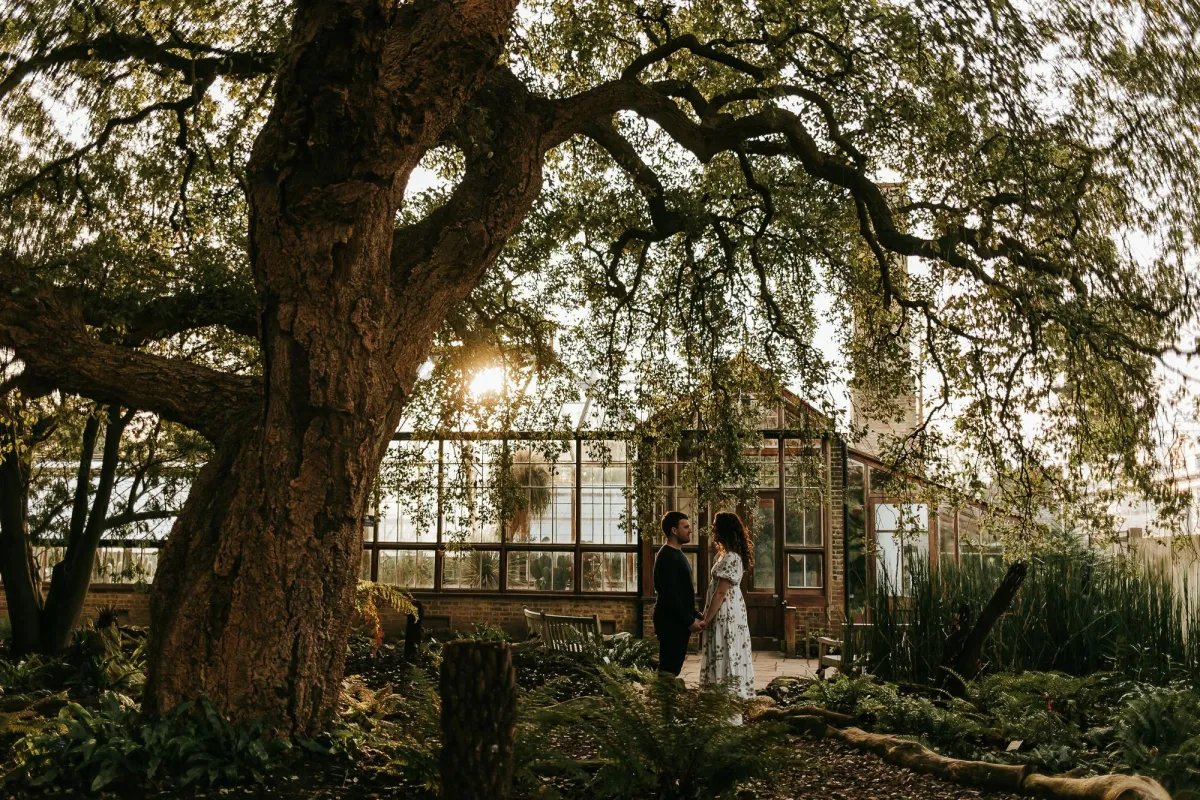 Photo of couple surrounded by trees and the Cambridge Botanical Gardens Green House behind them