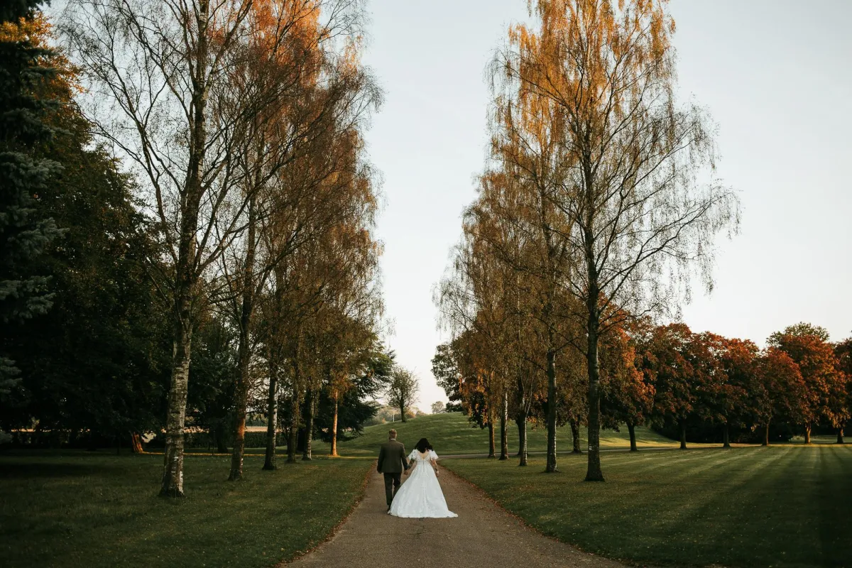 Photo of wedding couple walking down a road between tall trees at Haughty Park Wedding Venue