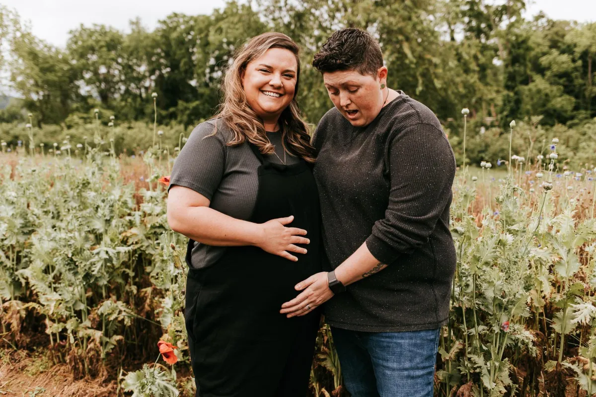 Photo of lesbian couple showing off their baby bump and looking really excited
