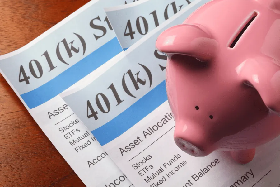 Pink piggy bank on top of 401(k) retirement plan statements showing asset allocation and investment options.