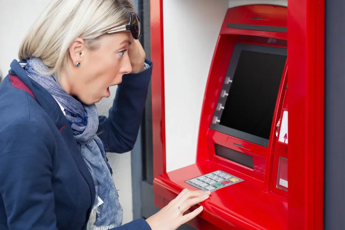 Shocked woman at ATM discovering her bank account frozen due to IRS wage garnishment.