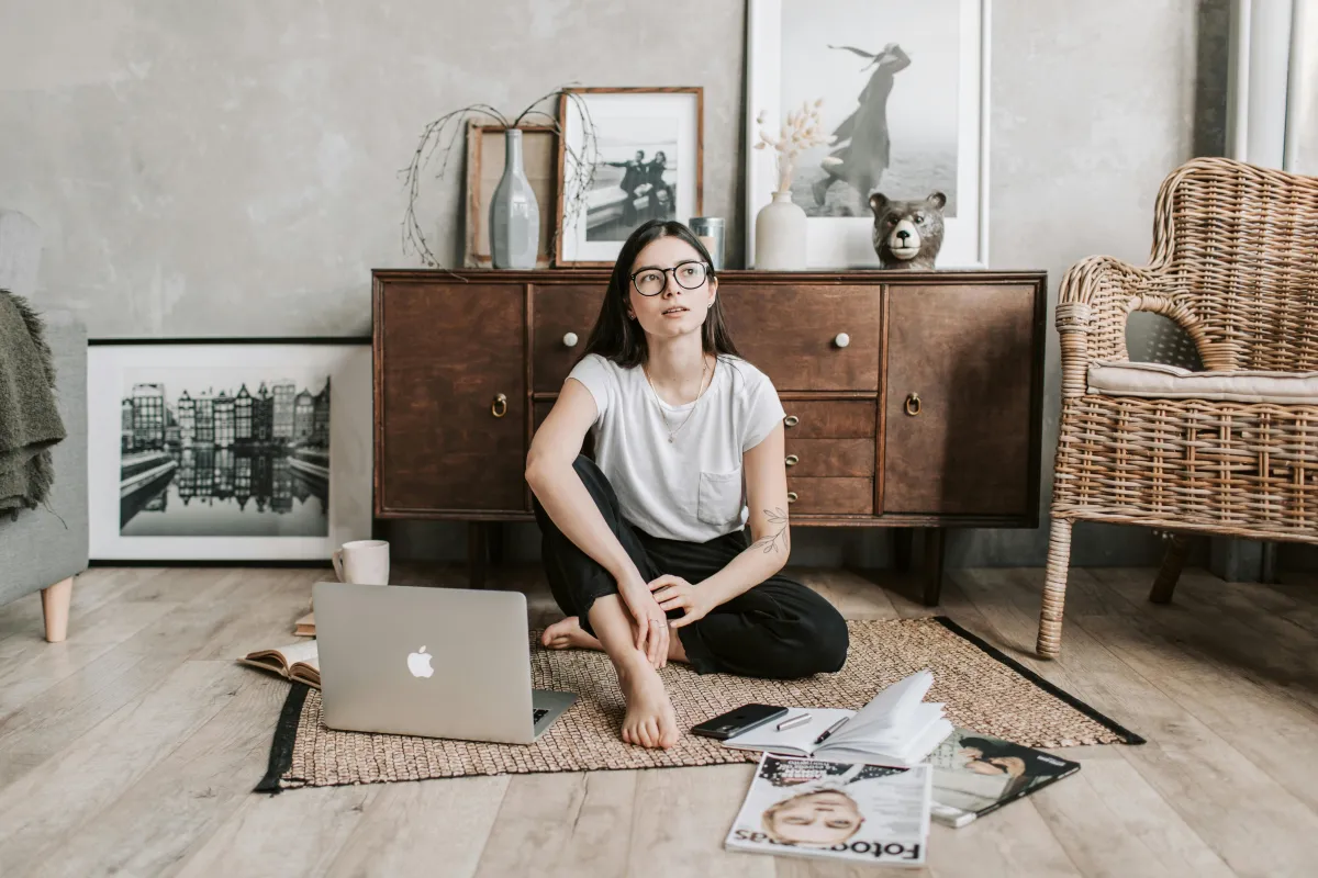 A woman sitting on the floor in a cozy, minimalist living room with a laptop, journal, and open book, surrounded by simple decor, symbolizing intentional living and inner calm.