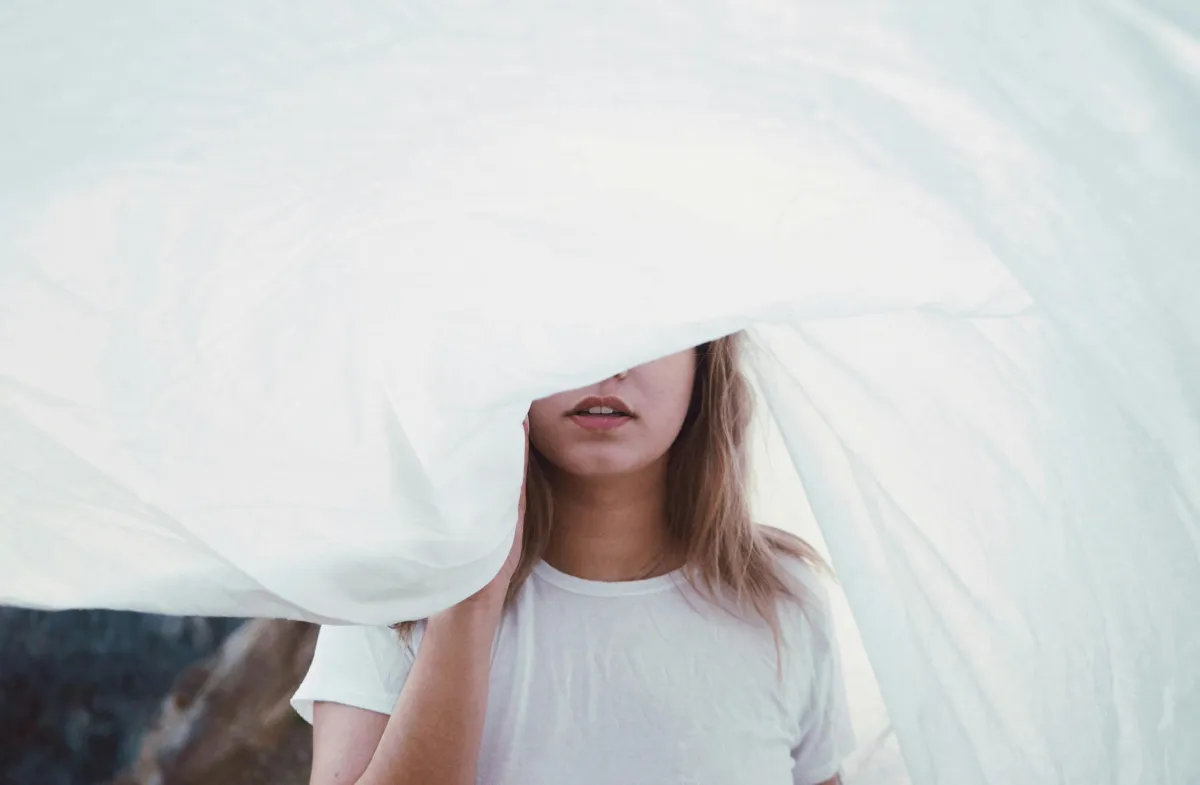 Close-up of a woman partially covered by white fabric, symbolizing overcoming limiting beliefs and unveiling personal potential.