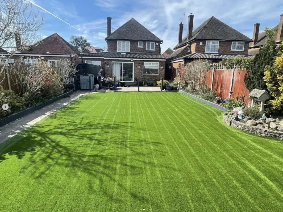 Striped artificial grass lawn in a rear garden with patio and shrubs