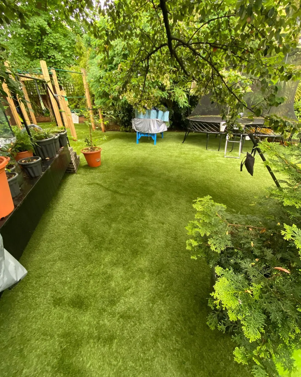 Artificial grass lawn under trees with pots, seating and garden equipment