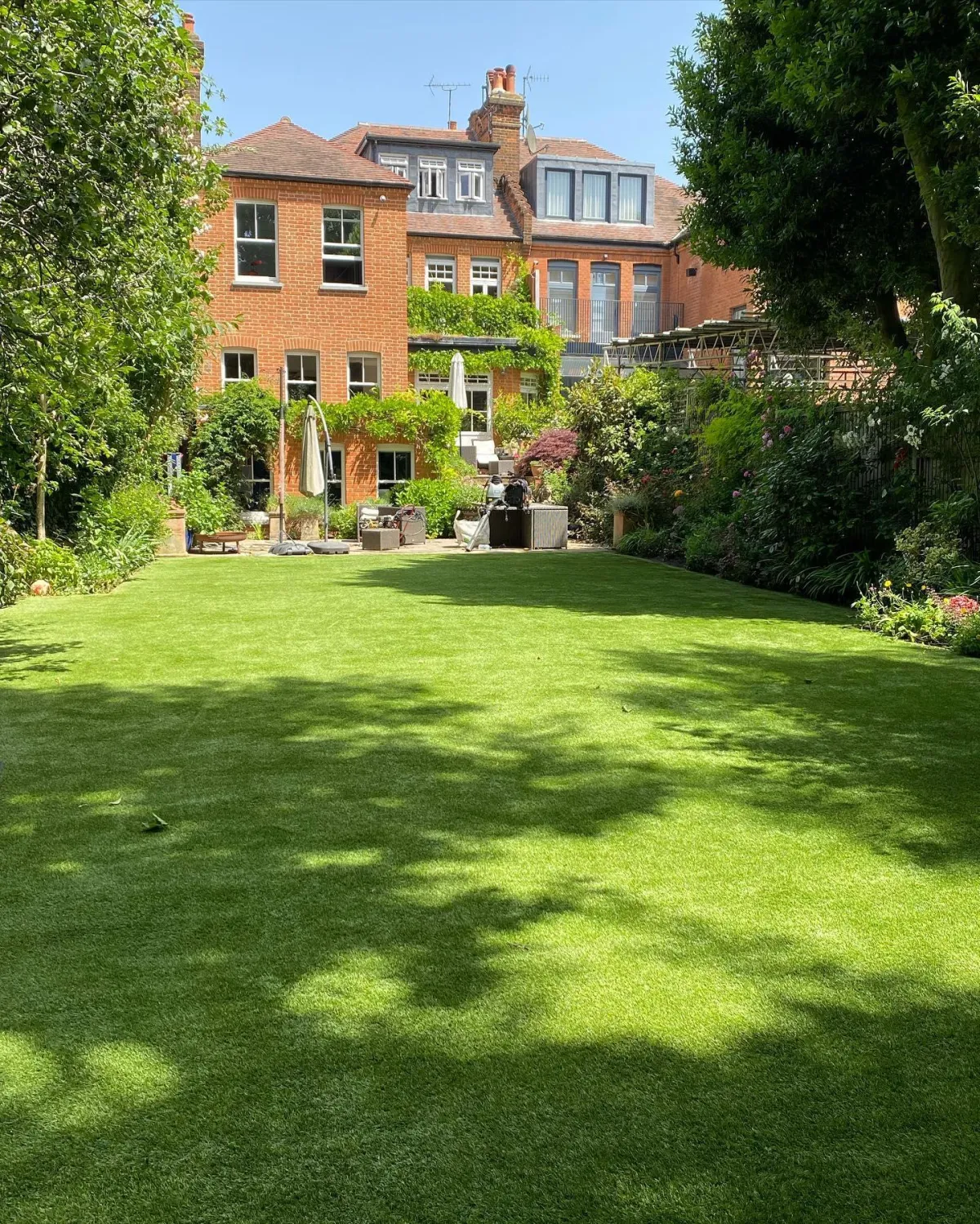 Large rear garden with artificial grass lawn and patio outside a brick house