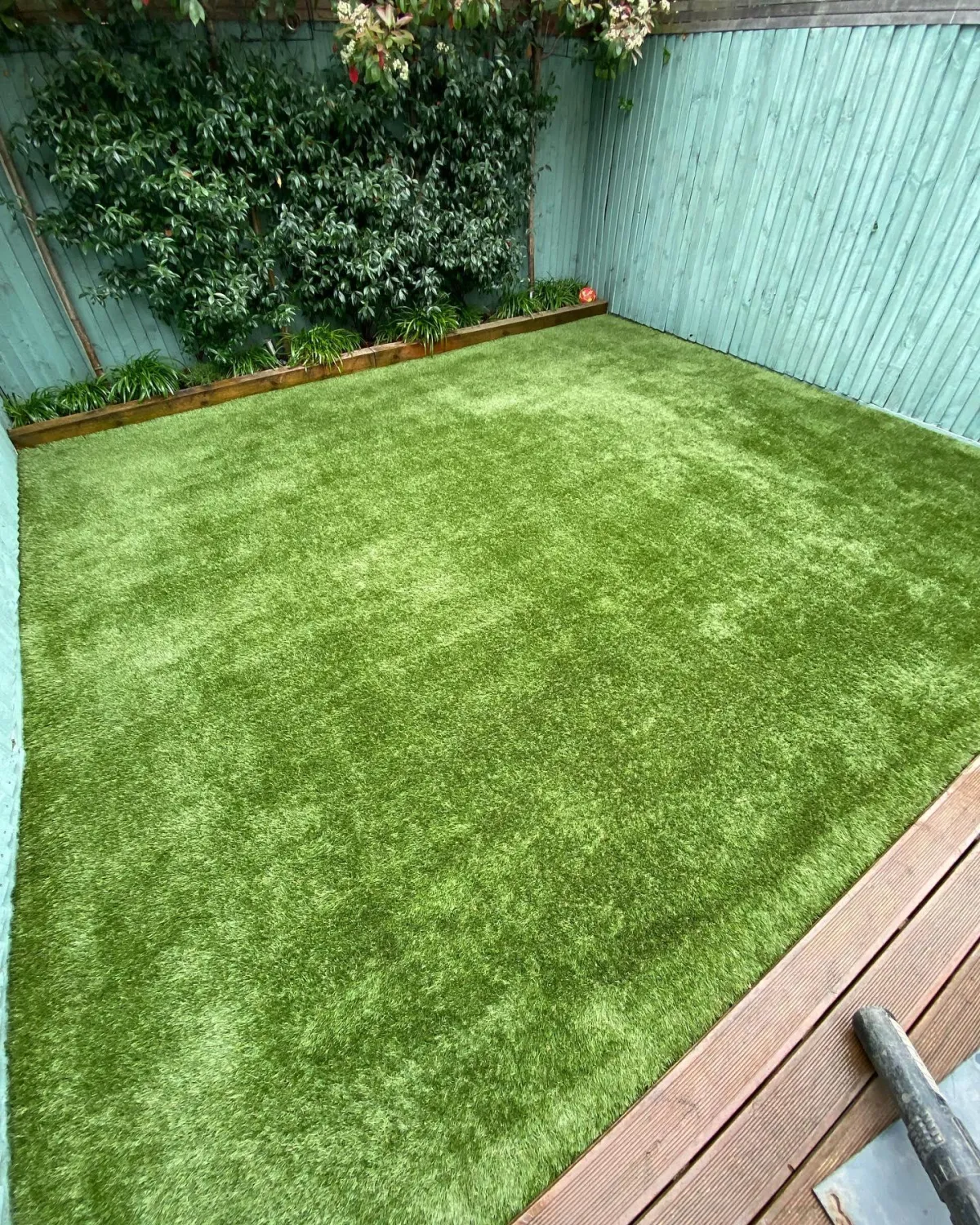 Small enclosed garden with artificial grass bordered by timber edging and painted fencing