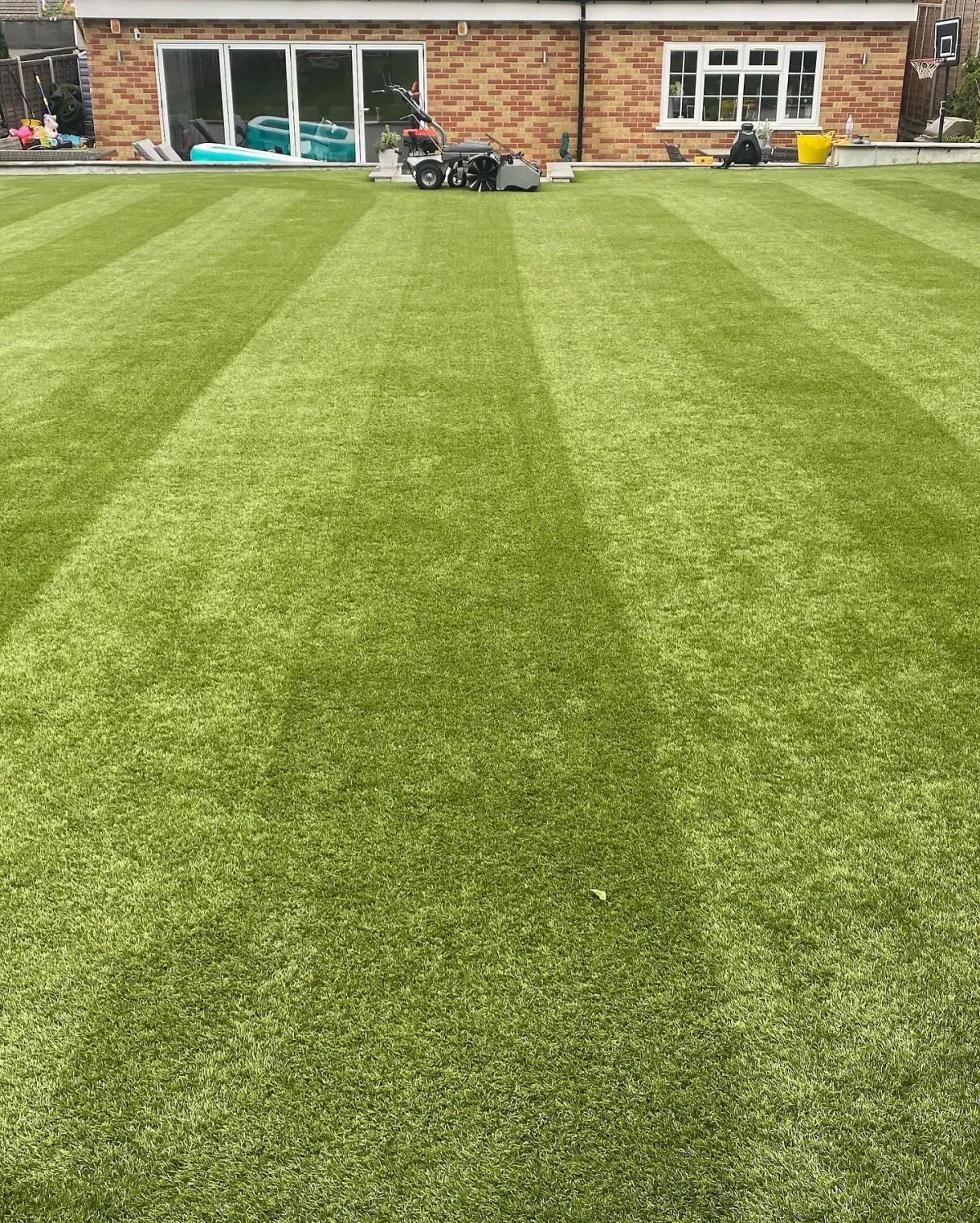 Wide artificial grass lawn with strong brushed stripes near a house and patio doors