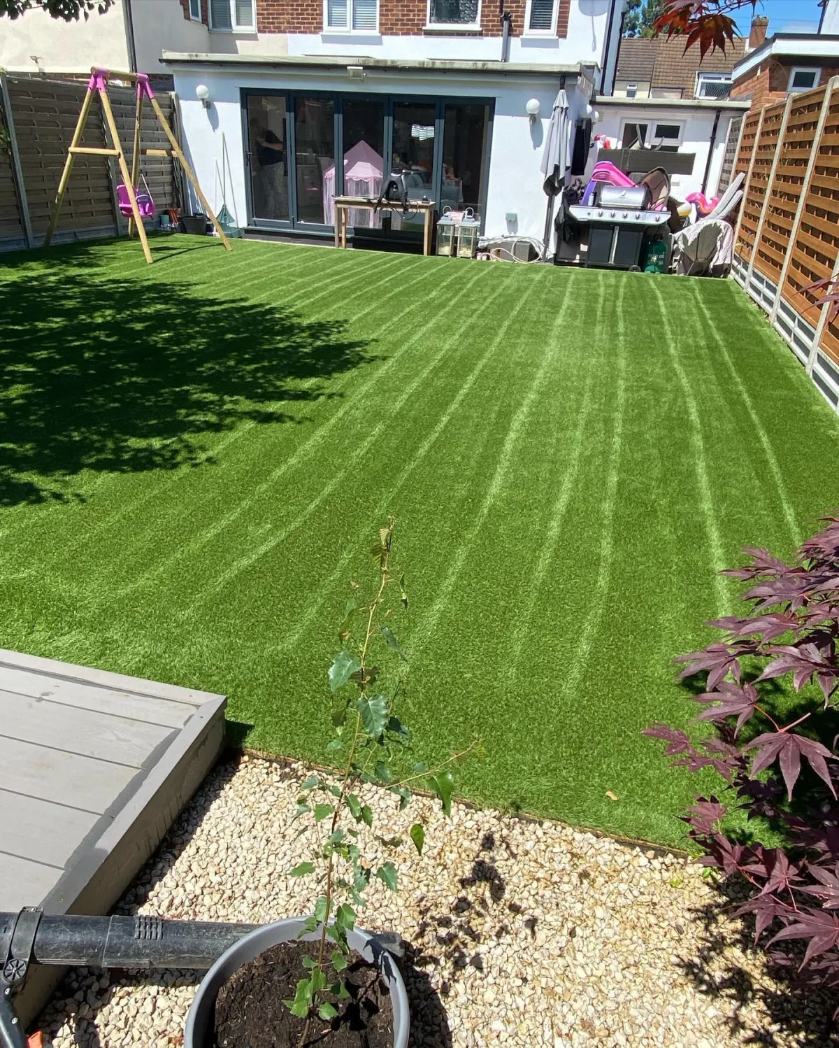 Artificial grass lawn with curved brushed stripes in a family garden with play equipment