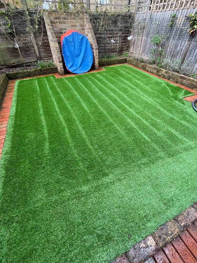 Small courtyard garden with striped artificial grass and brick edging