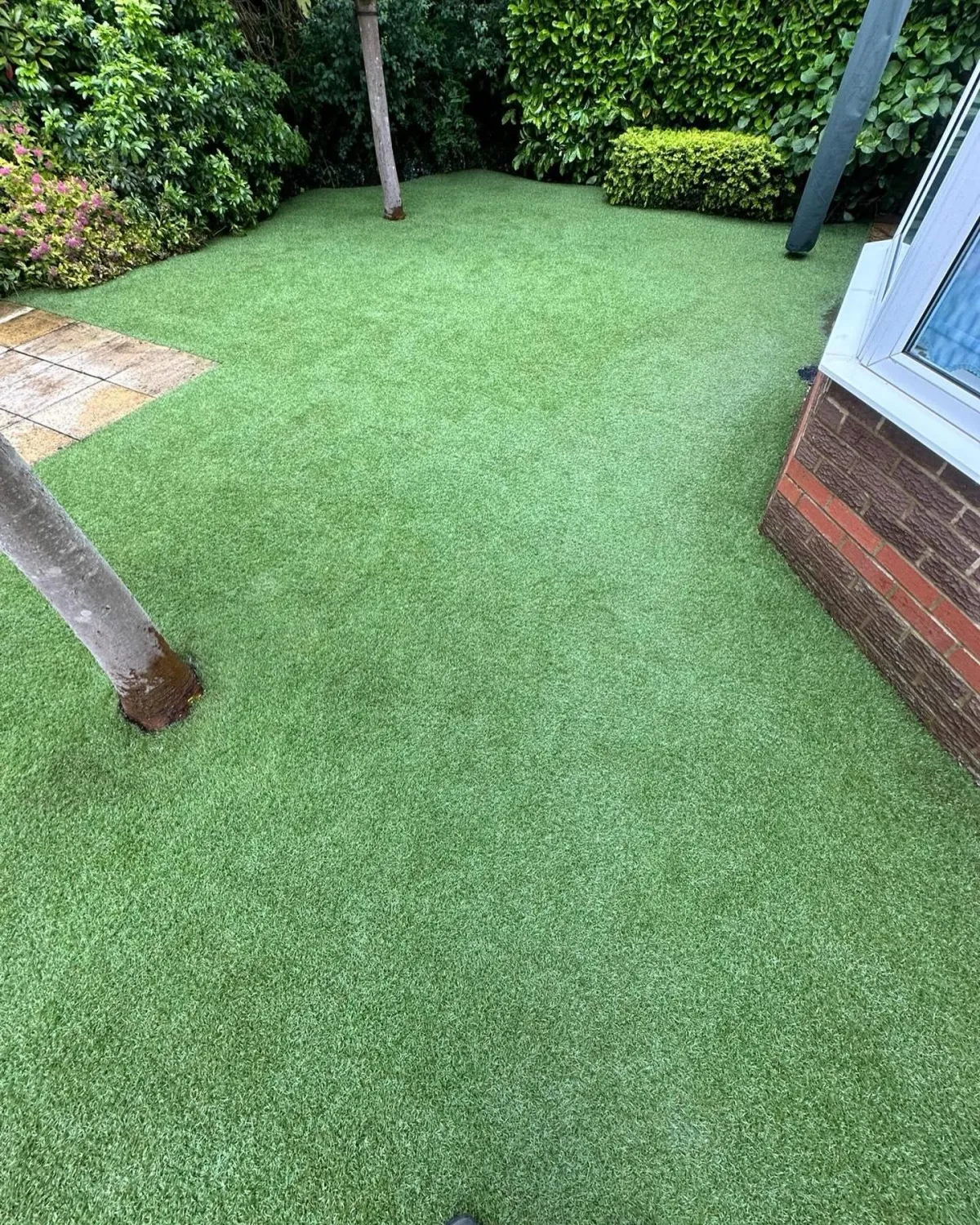 Artificial grass garden area next to a house with trees and dense shrubs