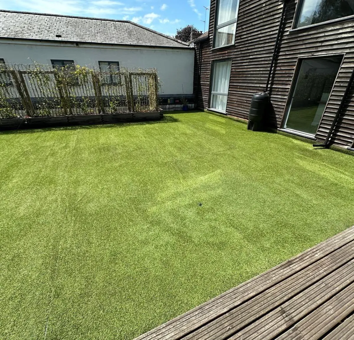 Large artificial grass area beside a modern timber-clad house and decking
