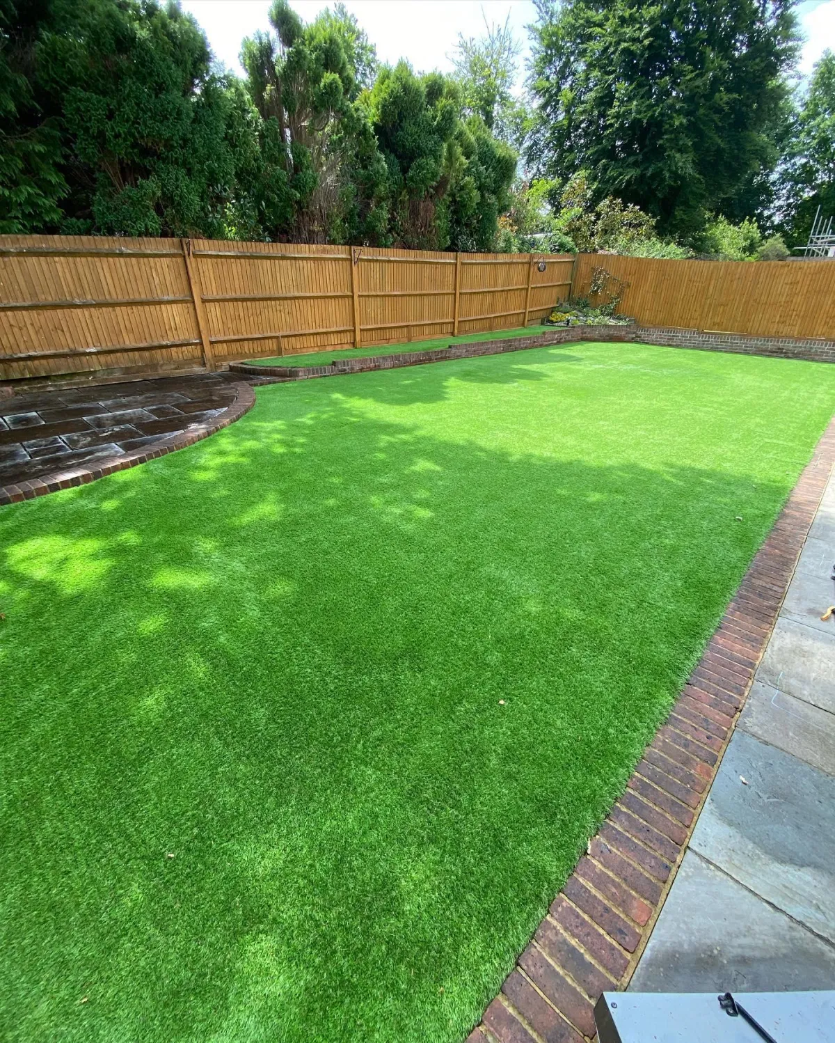 Back garden with artificial grass lawn, brick edging and timber fencing