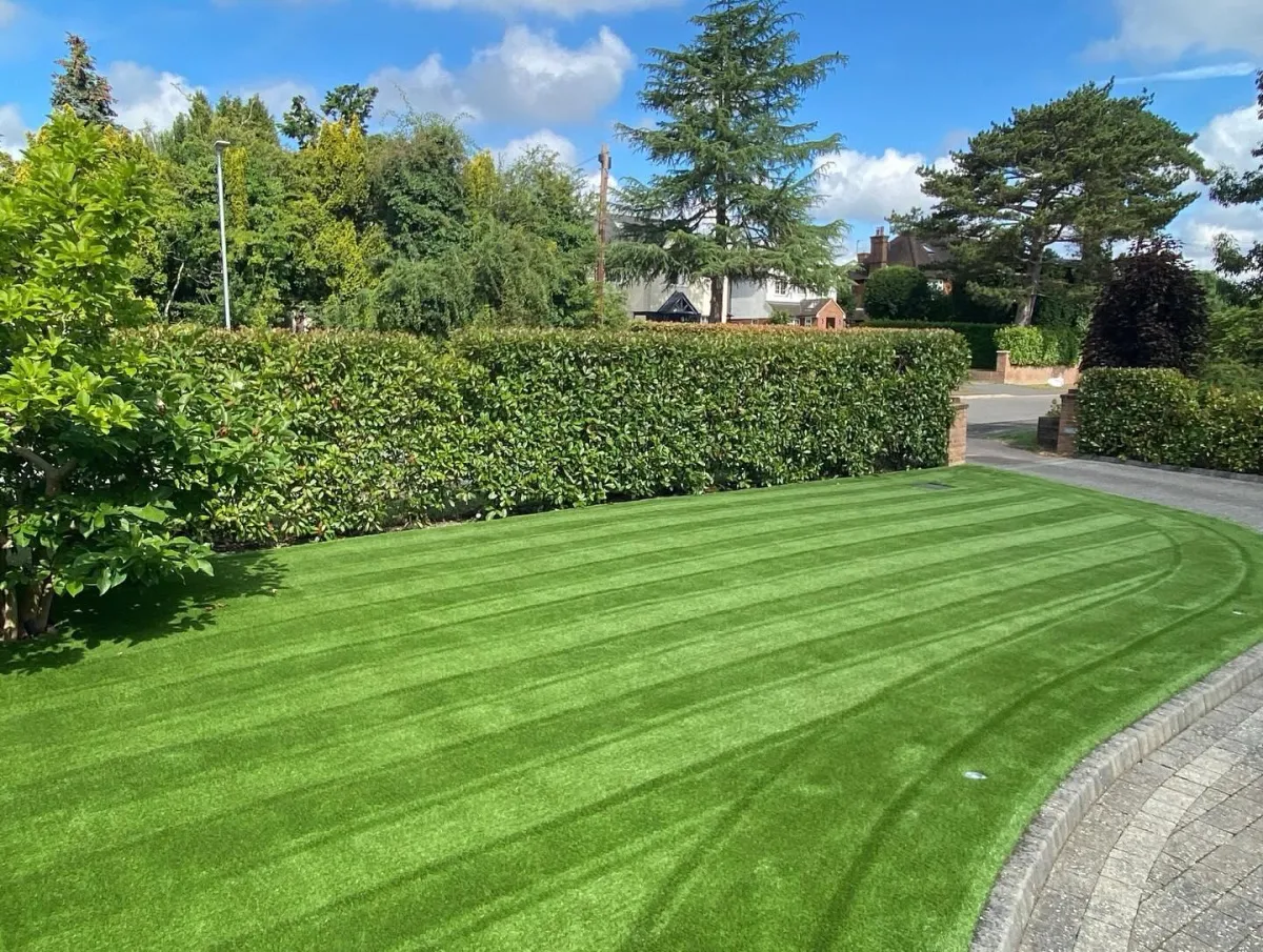 Front garden with striped artificial grass lawn bordered by hedging and paving