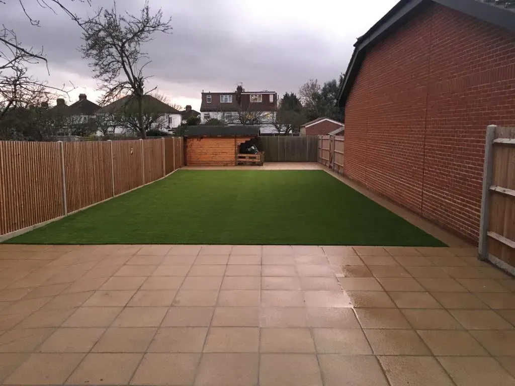 Artificial grass lawn with paved patio, fencing and brick wall in a long garden
