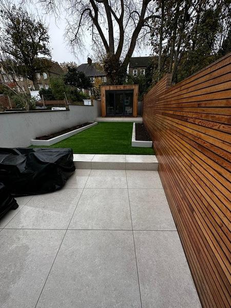Artificial grass lawn with grey tiled patio and timber slat fencing in a landscaped back garden.
