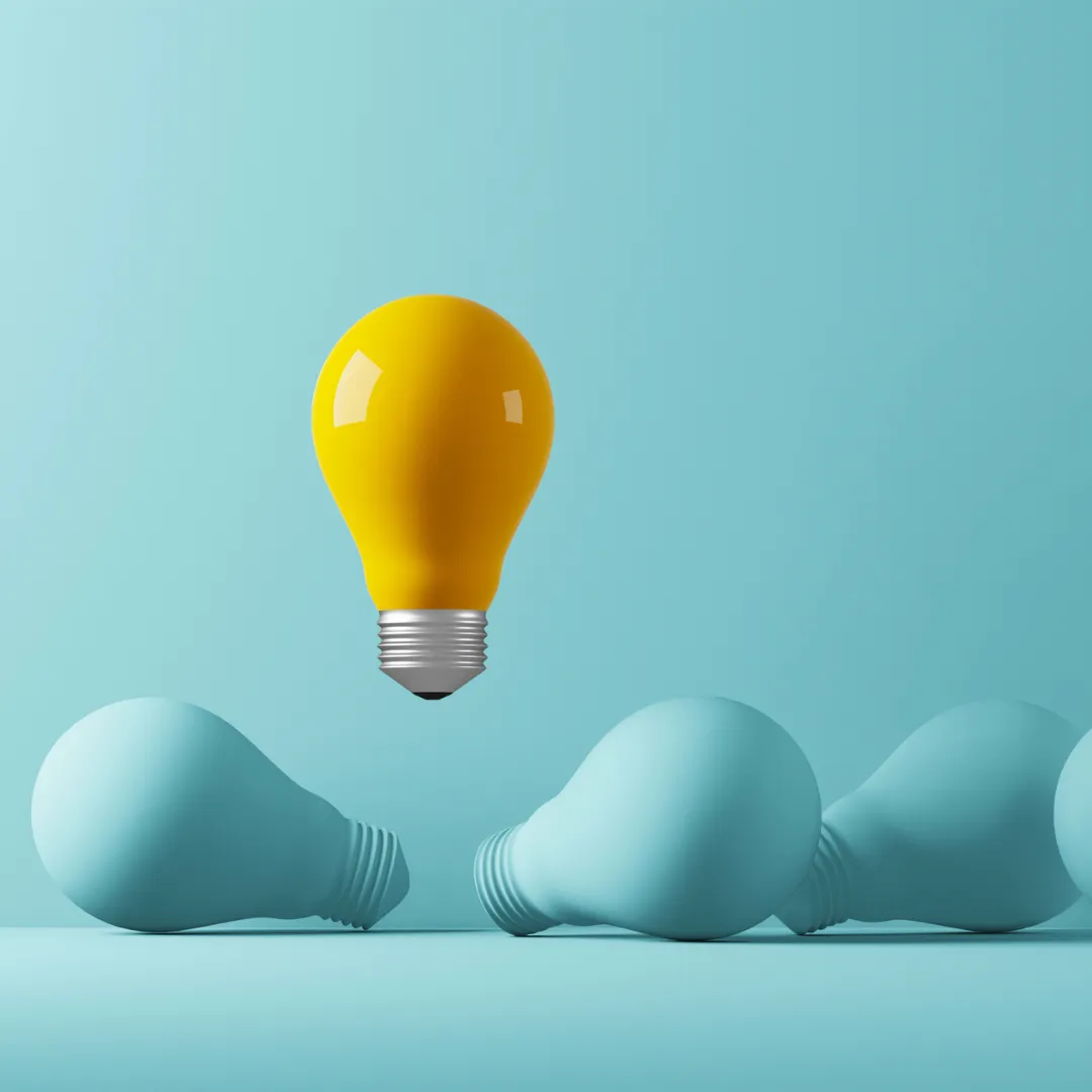 a yellow lightbulb floating above a set of monochromatic lightbulbs