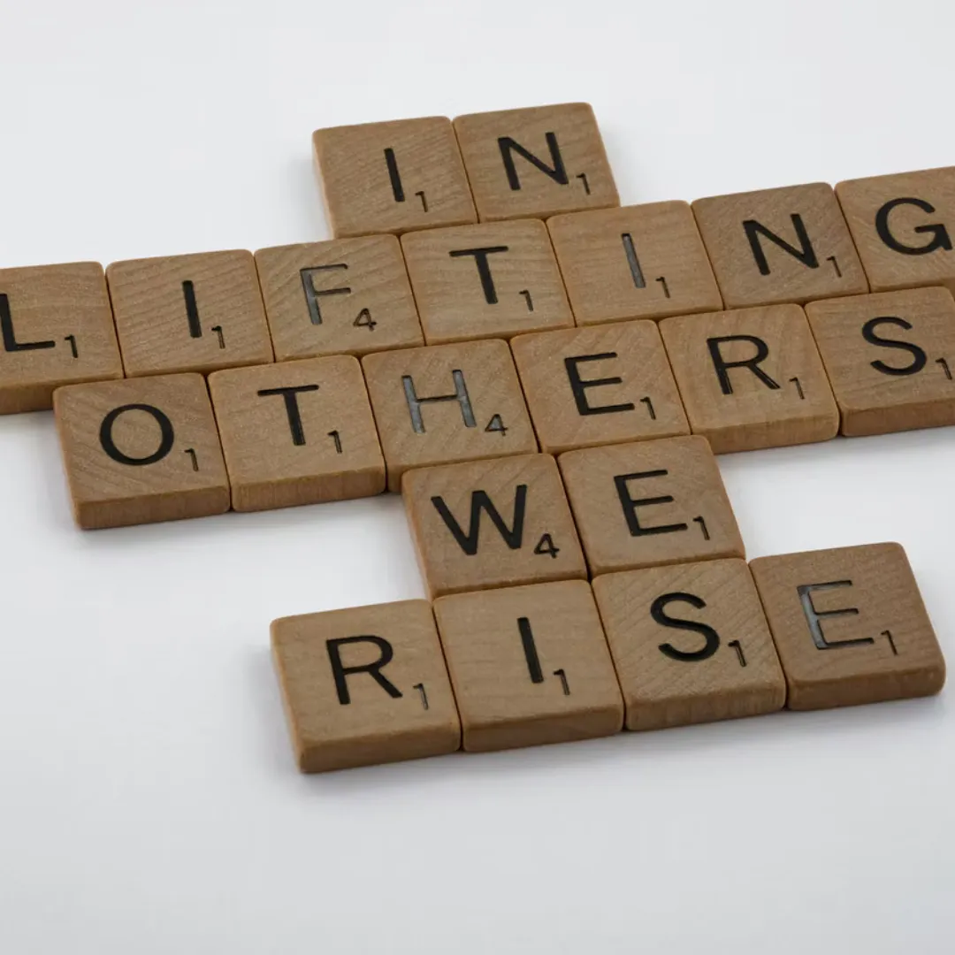 scrabble pieces that state the phrase, in lifting others we rise