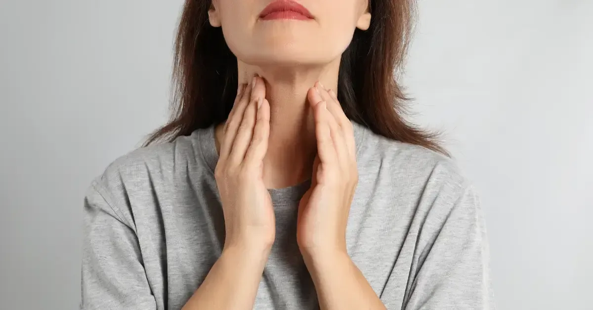 Close-up of a woman touching her neck, showing symptoms of low thyroid and hypothyroidism, a condition affecting hormone levels and requiring proper diagnosis and treatment.