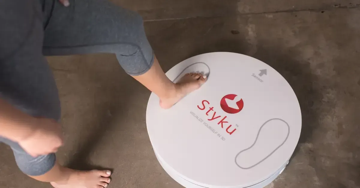 Person stepping onto a Styku 3D body scanner platform, starting a high-tech scan to measure body composition and track fitness progress.