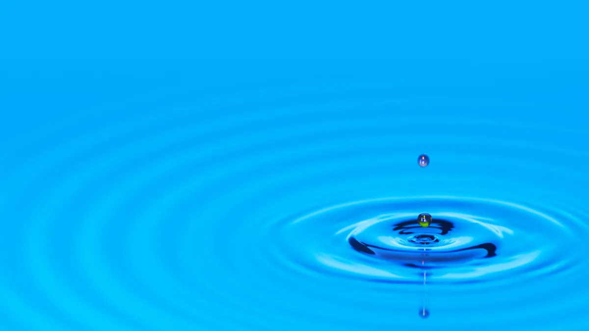 A drip rippling into a calm area of blue water making circles