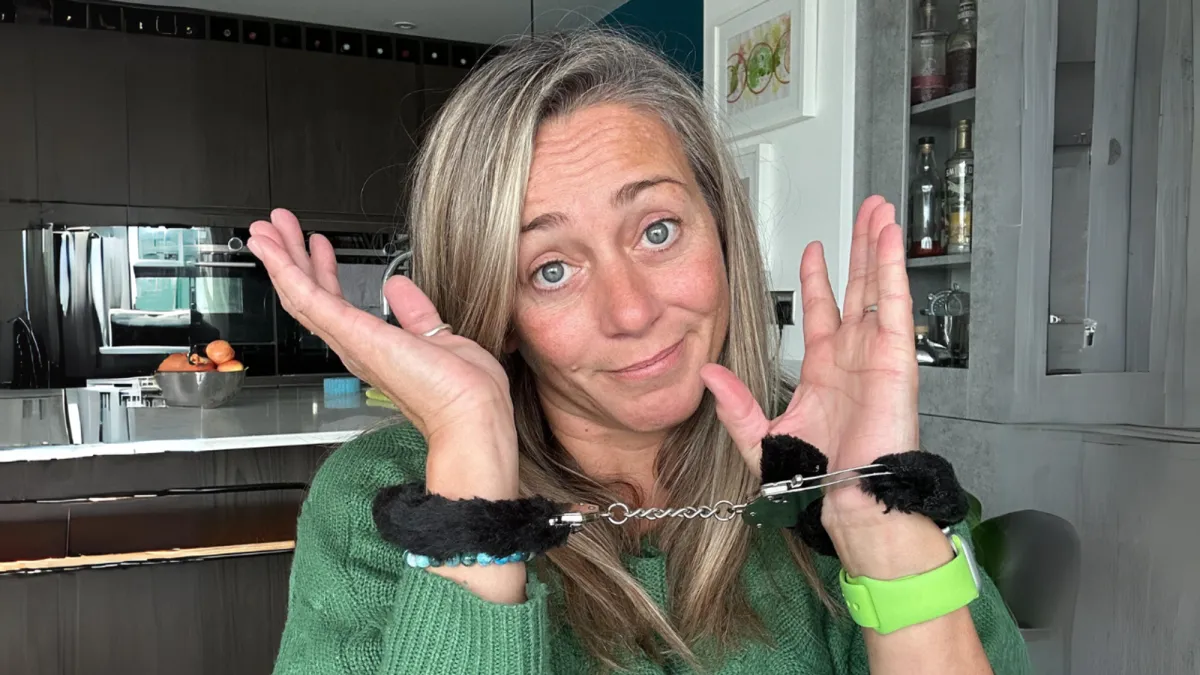 Blonde-haired, blue-eyed woman holding her hands in front of her face wearing fluffy handcuffs