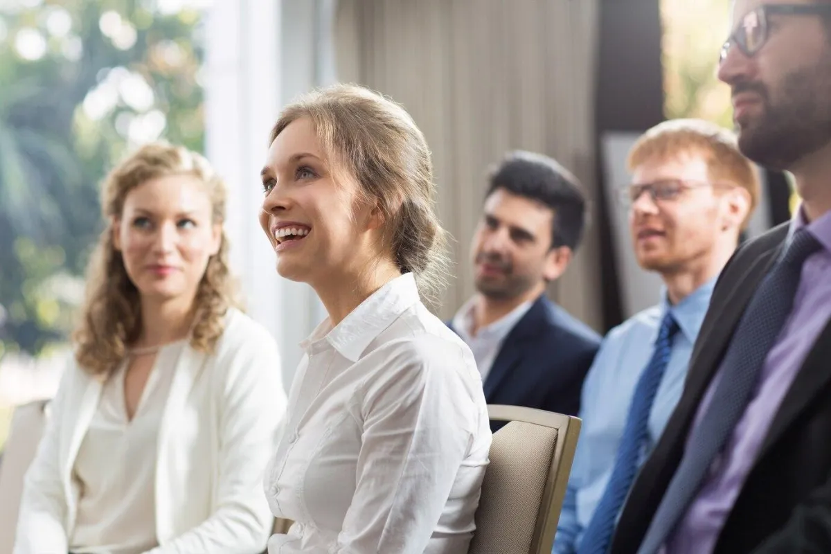 Woman sitting and smiling with other people around her - Speak up and inspire action