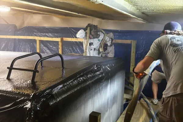 Technicians applying spray foam insulation coating for industrial roof and equipment protection.