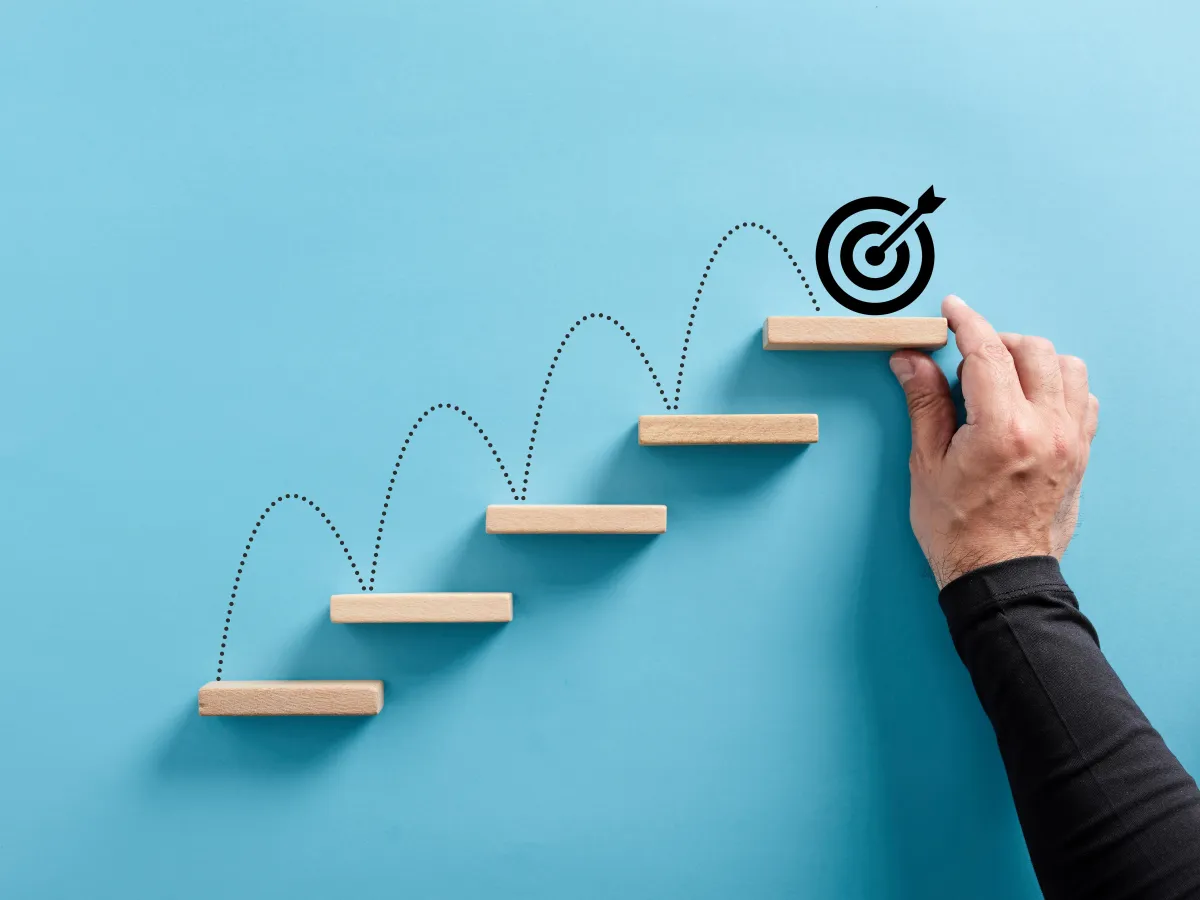 Hand arranging a wooden block staircase with a target icon, symbolizing goal setting or achieving objectives.