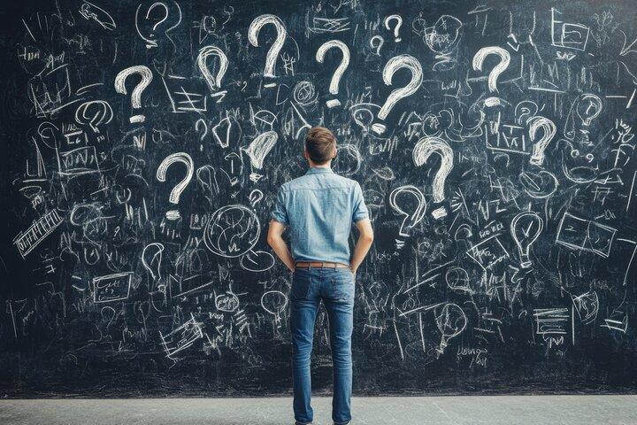 Man standing in front of chalkboard filled with question marks and sketches, symbolizing confusion about the cause of autism and search for answers beyond a cure.