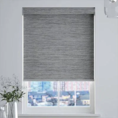 A dark gray blackout roller shade pulled completely down over a bedroom window during the day.