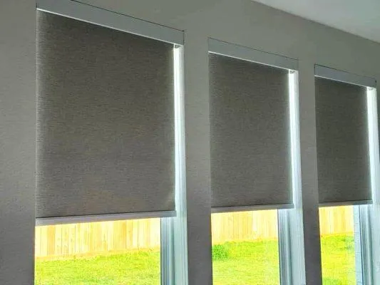 A neutral-colored light-filtering roller shade on a large window in a bright, modern living room in Houston, TX.