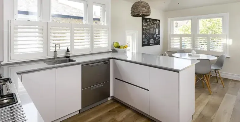 A dining nook with a table and chairs, featuring white Café Style Shutters on the window.