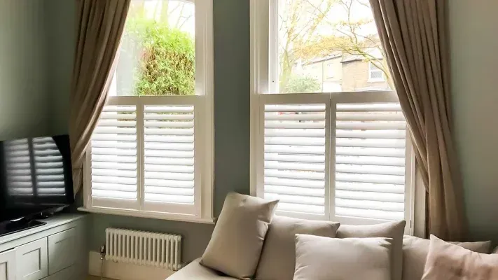 A living room window with Café Style Shutters on the lower half and unfiltered light streaming in from the top.