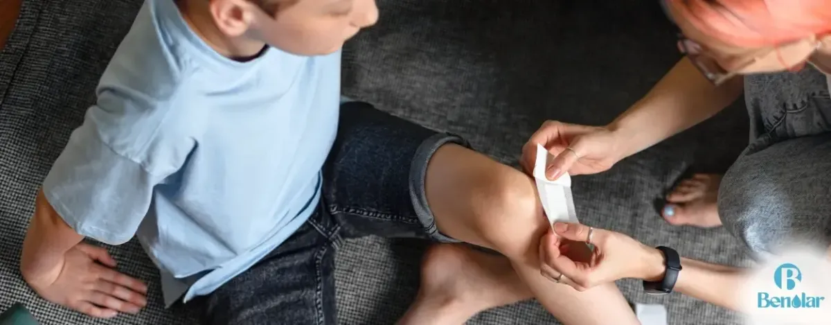 applying a band-aid to a kids knee with Benolar on it