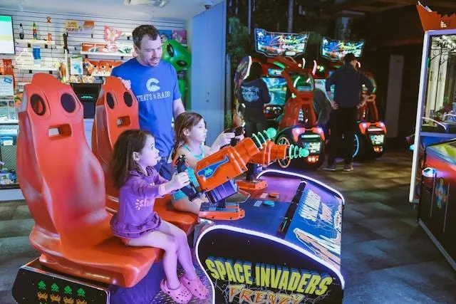 Two children playing space invaders while father watches