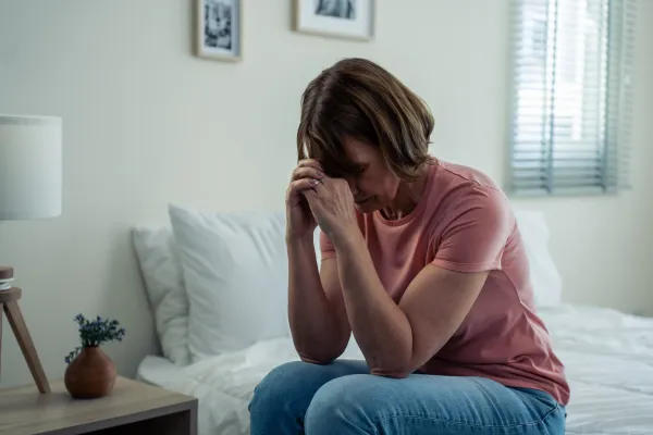 Middle-aged woman sitting on bed with head in hands, feeling stressed during a challenging season in her marriage.